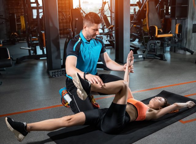 trainer assisting woman doing dead bug exercise in gym