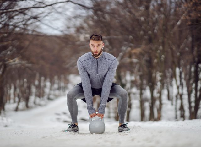 man doing squats outside with kettlebell