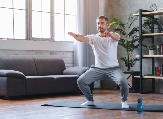 man in his 50s does squat on yoga mat