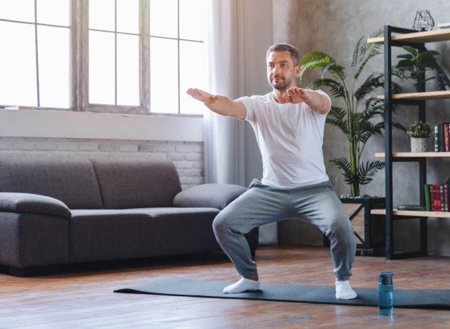 man in his 50s squats on a yoga mat