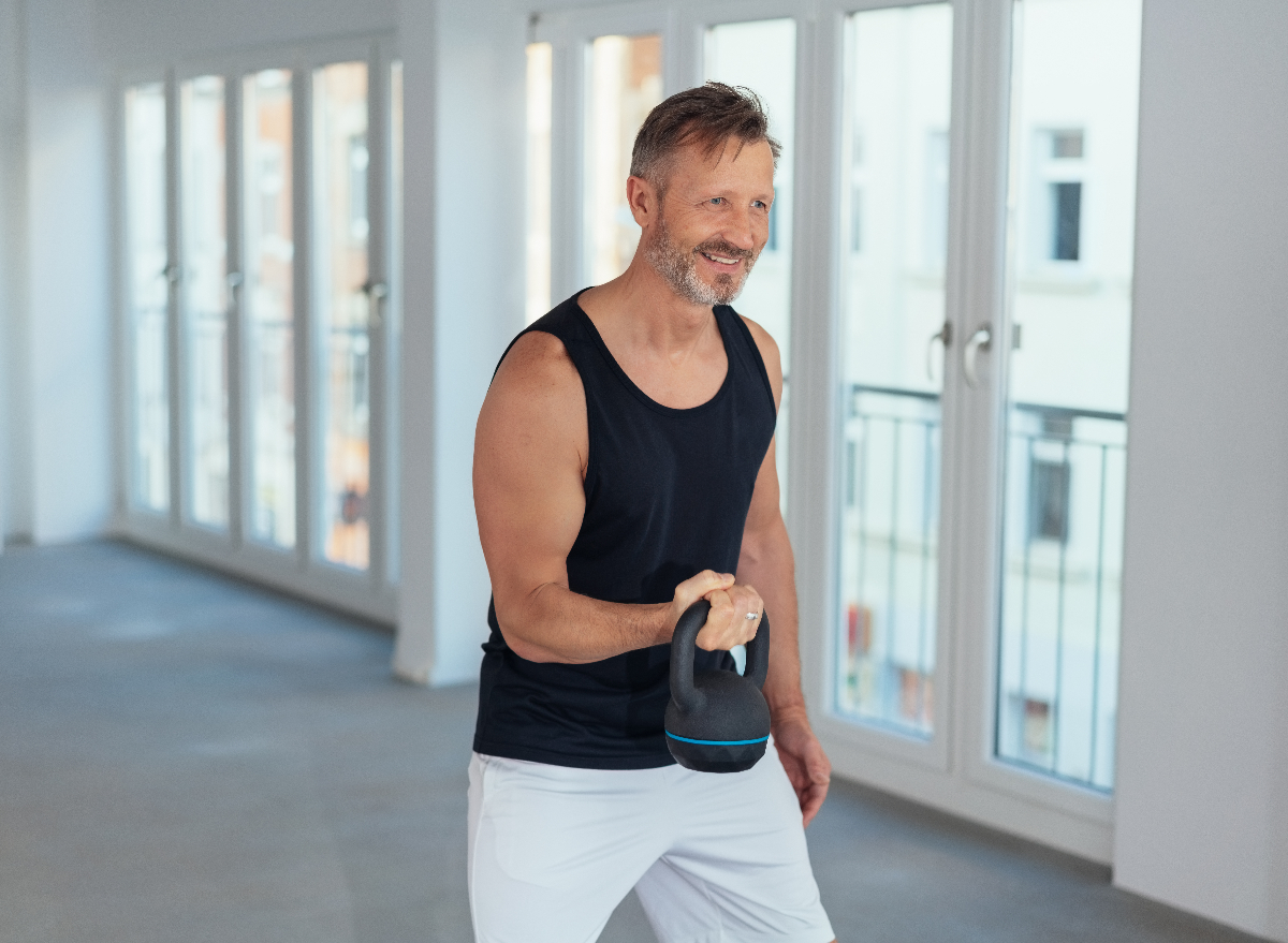 man doing kettlebell workout in bright apartment