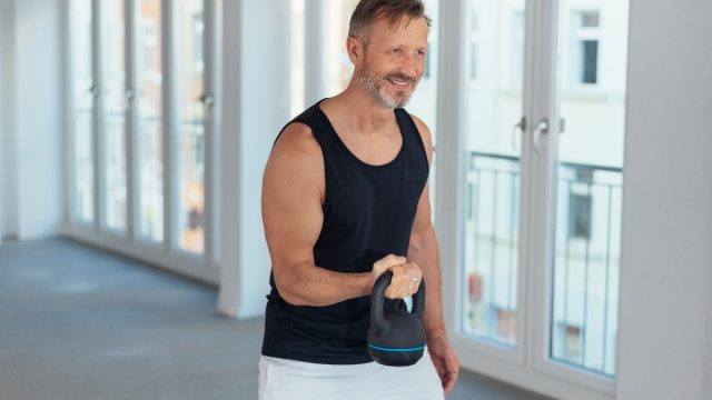 man doing kettlebell workout in bright apartment