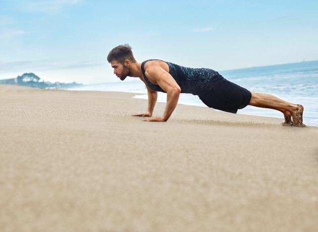 man doing pushups at beach in sand