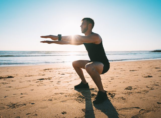 man doing squats at the beach