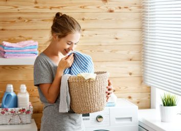 happy woman smelling clean laundry next to washing machine