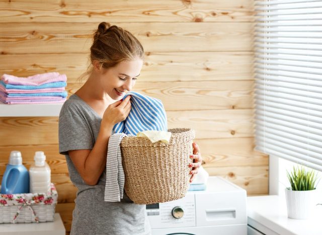 happy woman smelling clean laundry next to washing machine