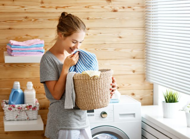 happy woman smelling clean laundry next to washing machine