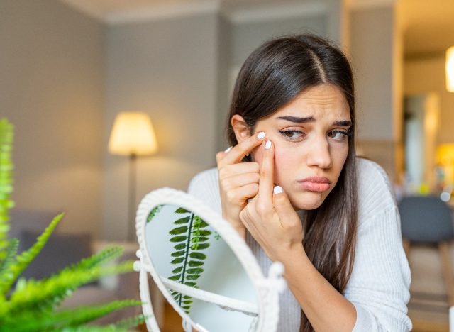 woman popping pimple in mirror