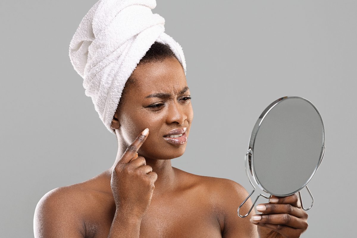 woman looks in mirror at pimple