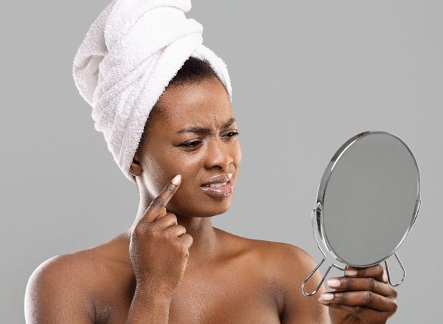 woman looks in mirror at pimple