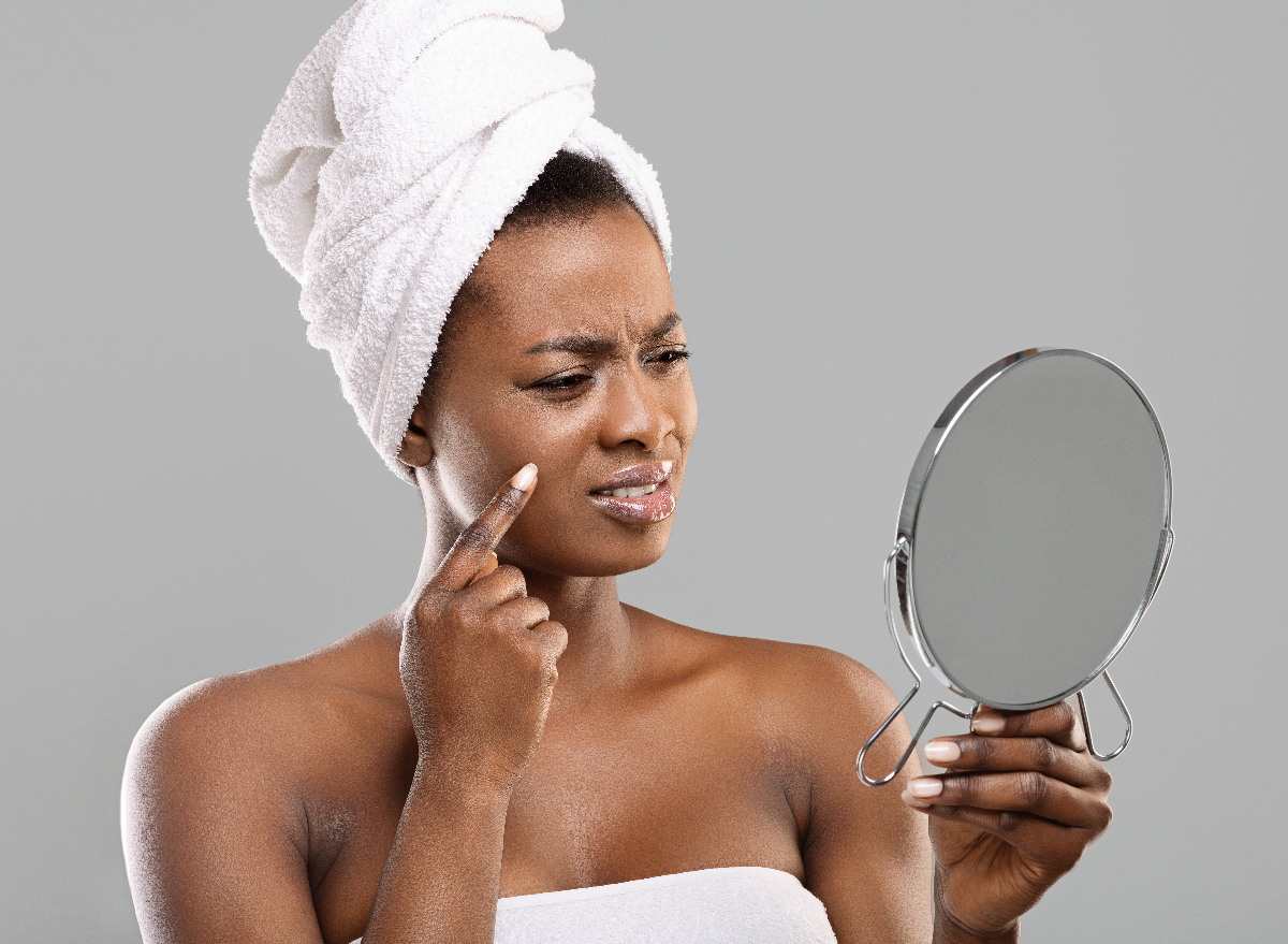 woman looks in mirror at pimple
