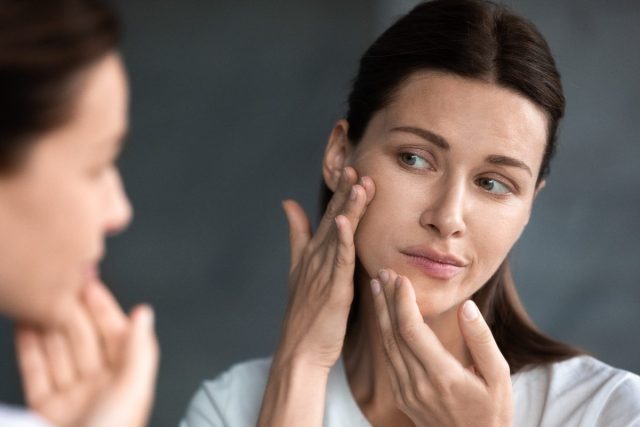 woman looking at pimple on skin