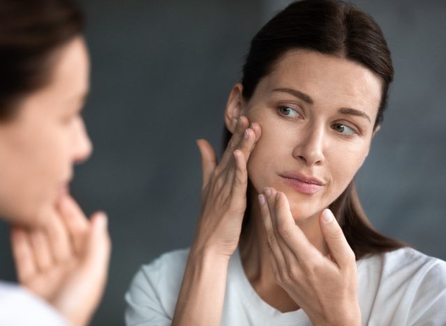 woman looking at pimple on skin