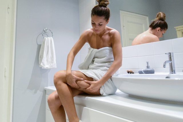 Femme regardant la cellulite sur la jambe dans la salle de bain