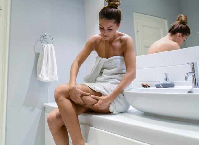 woman looking at cellulite on leg in bathroom