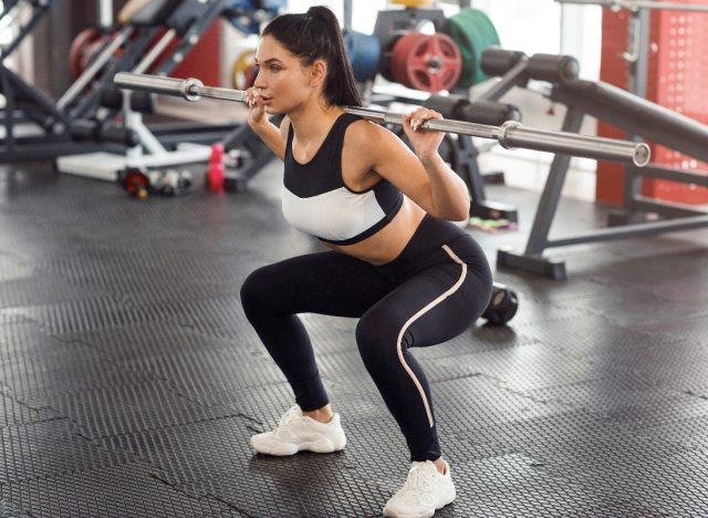 woman doing barbell squat in gym