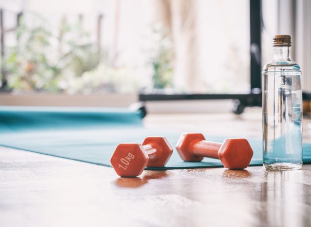 yoga mat rolled out with dumbbells and water bottle