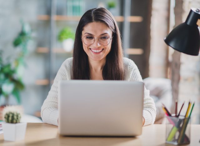 happy woman types on laptop in work from home setup