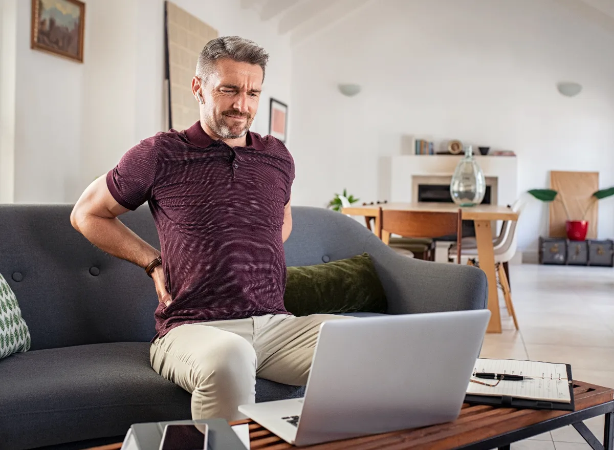 man bad back sitting on couch while working
