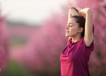 woman in pink shirt is relaxed as she stretches outside