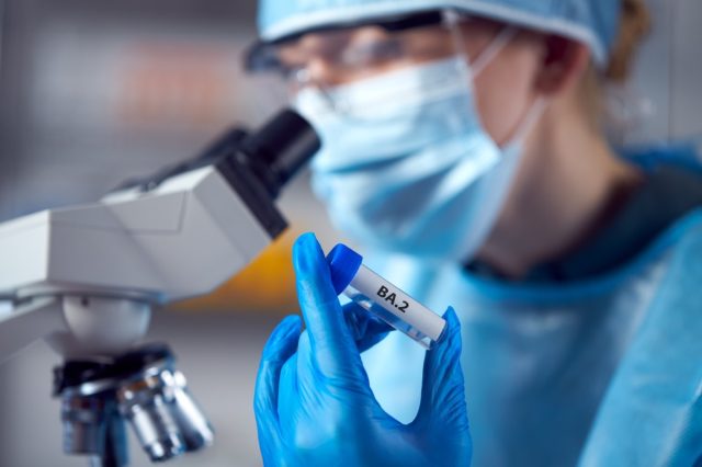 Female lab researcher in PPE clothes is holding test tube labelled BA.2.