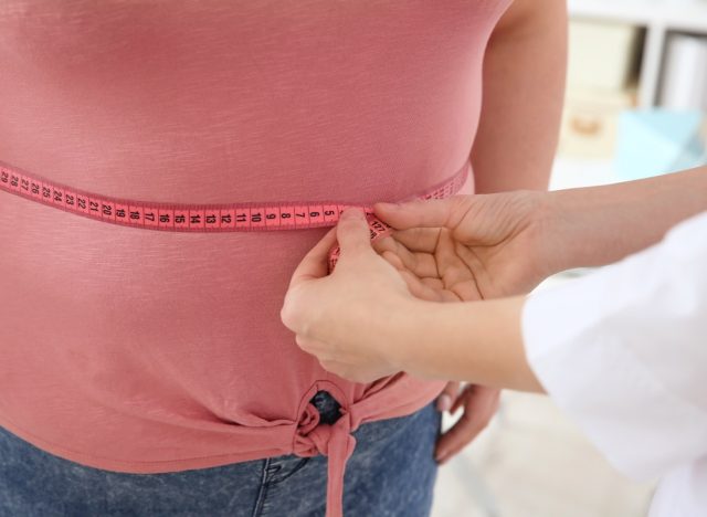 Female doctor measuring waist of overweight woman with measuring tape in clinic
