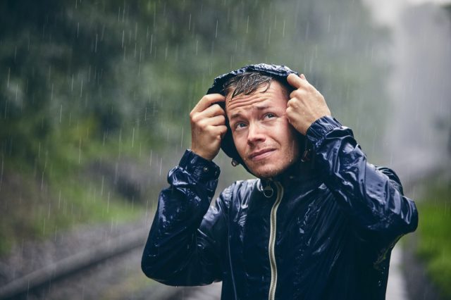 Portrait of young man in drenched jacket in heavy rain.
