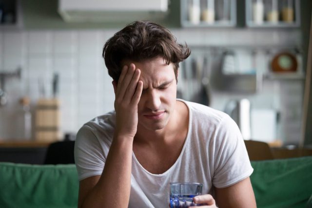 man with headache holding water