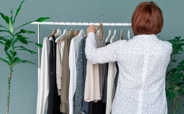 Middle Aged Woman makes shopping and looks at the new dress near shelf with clothes.