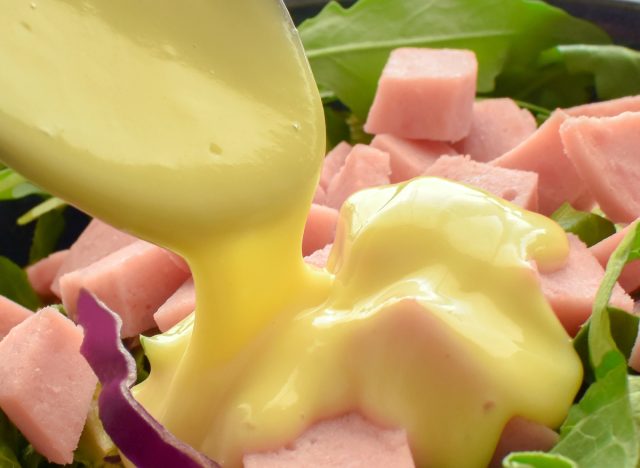 pouring creamy salad dressing on salad with ham