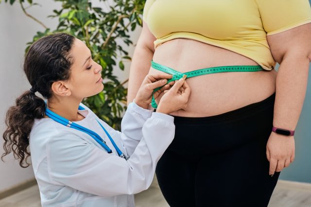 Nutritionist inspecting a woman's waist using a tape measure to prescribe a weight loss diet