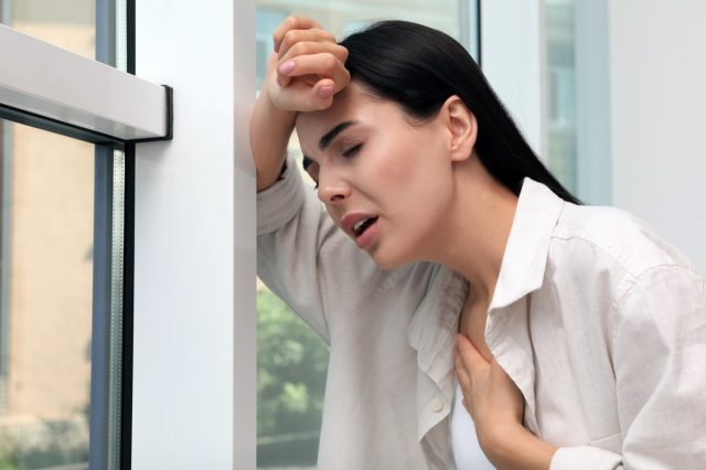 Young woman suffering from breathing problem near window indoors.