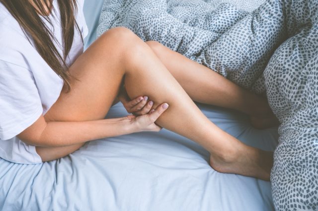 Frau liegt im Bett und leidet unter Muskelkrämpfen in den Beinen