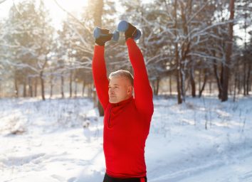 man doing exercise with dumbbells outdoors along winter walk