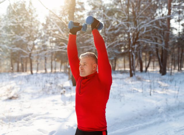 man doing exercise with dumbbells outdoors along the winter promenade