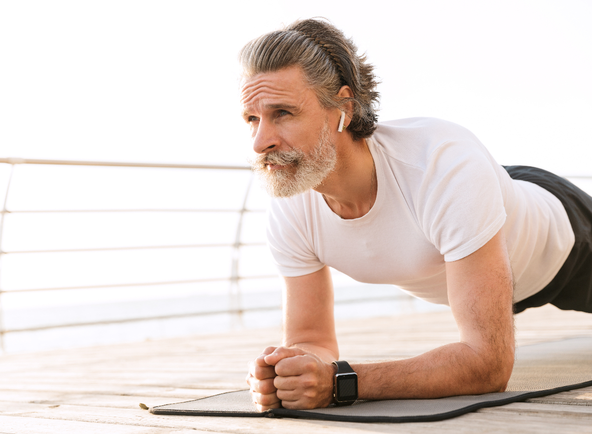 senior man doing plank outdoors on boardwalk, sunny day