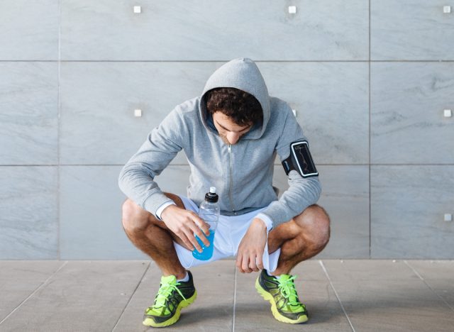 man kneeling down holding energy drink post-workout