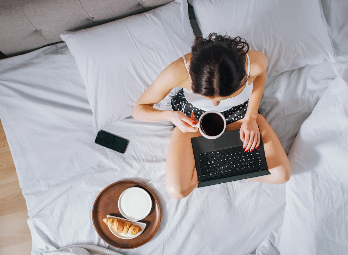 woman working from bed with coffee, laptop, and croissant