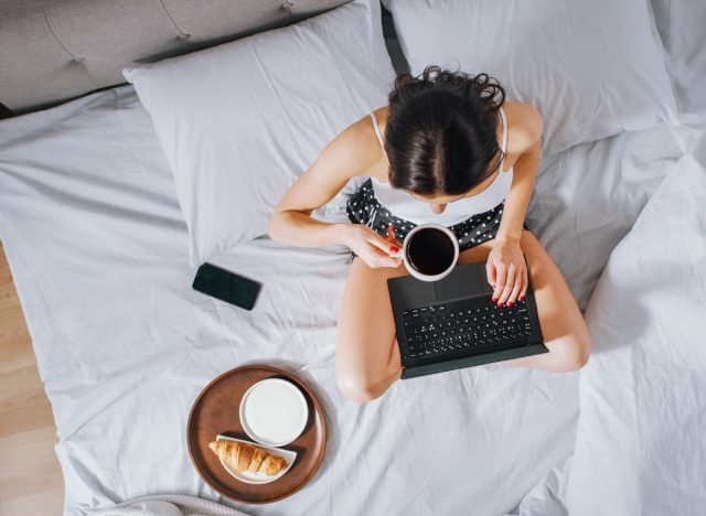 woman working from bed with coffee, laptop, and croissant