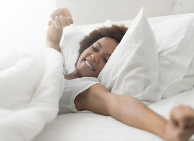 happy woman stretches in bed