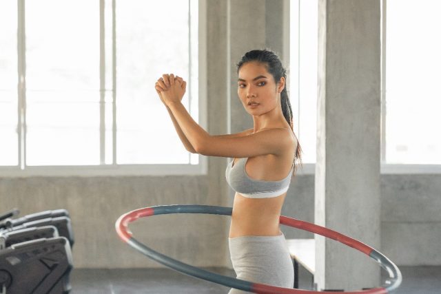 woman working out with weighted hula hoop in gym