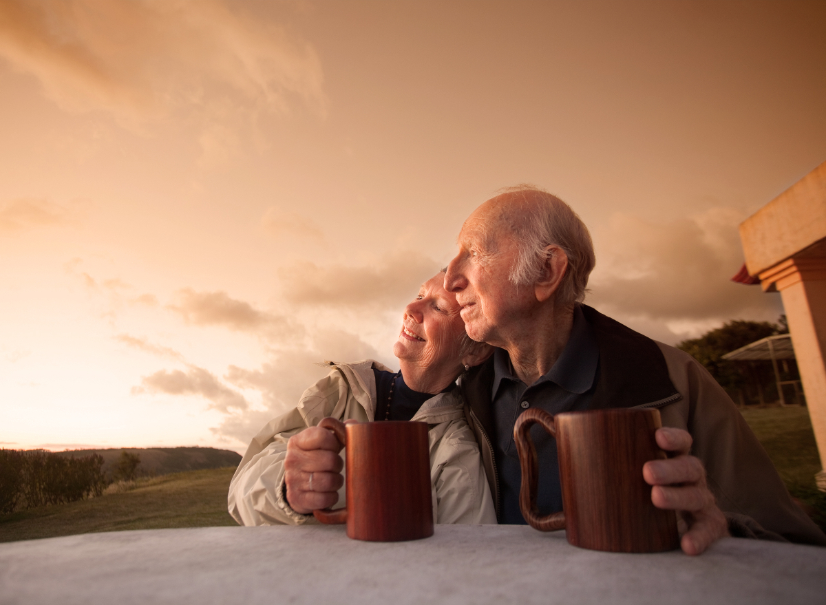 elderly couple cuddles up outside while enjoying morning coffee
