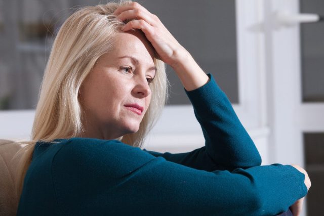 woman sits on the couch, tired, while dealing with menopause