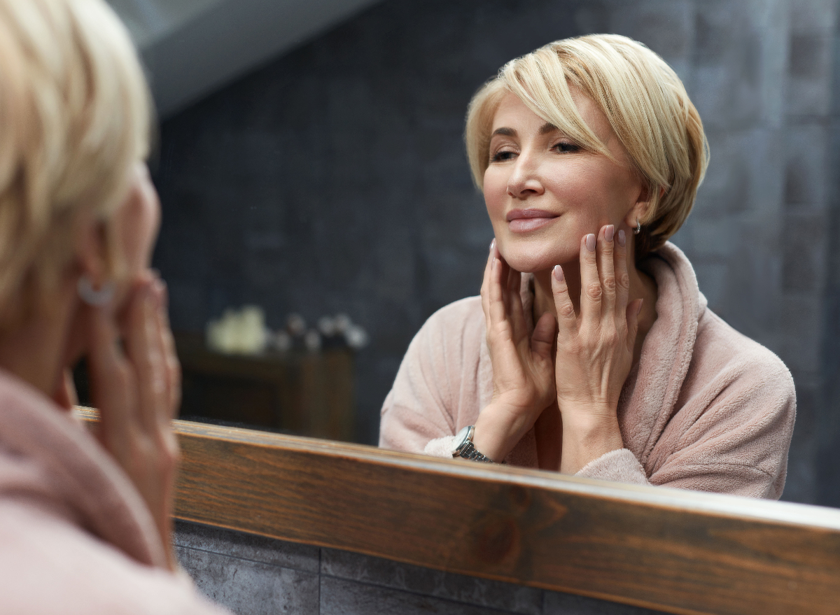 woman smiles at reflection in bathroom mirror, glowing skin