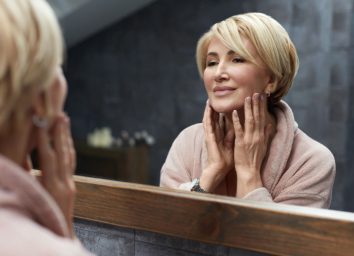 woman smiles at reflection in bathroom mirror, glowing skin