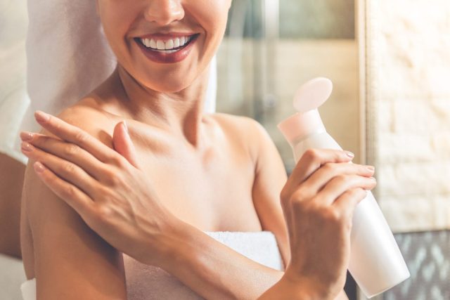 woman applying lotion to arm after shower