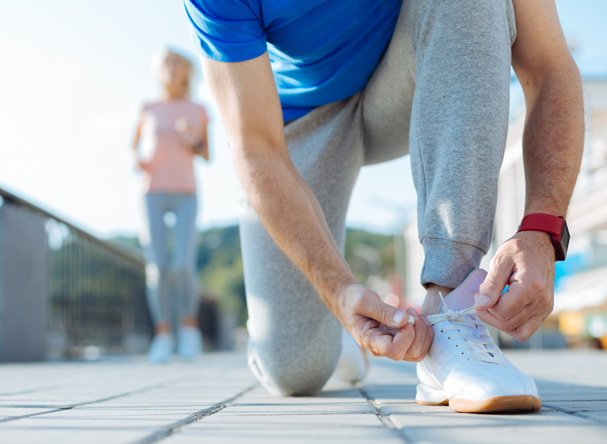 older man tying sneakers while on a walk outside