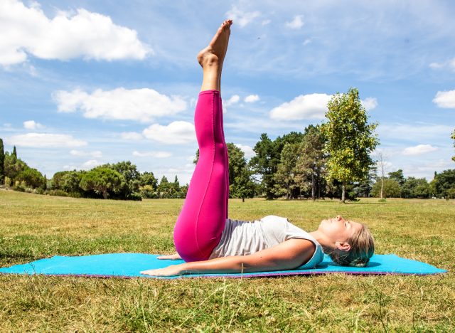 Woman doing leg raises outdoors on a sunny day on a yoga mat