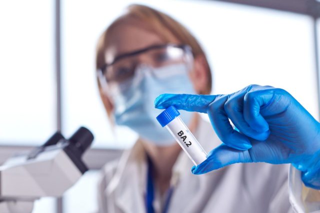 Female Lab Research Worker Wearing PPE Holding Test Tube Labelled BA.2
