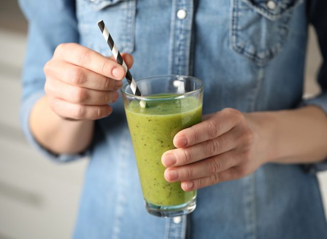 holding a green smoothie with a straw